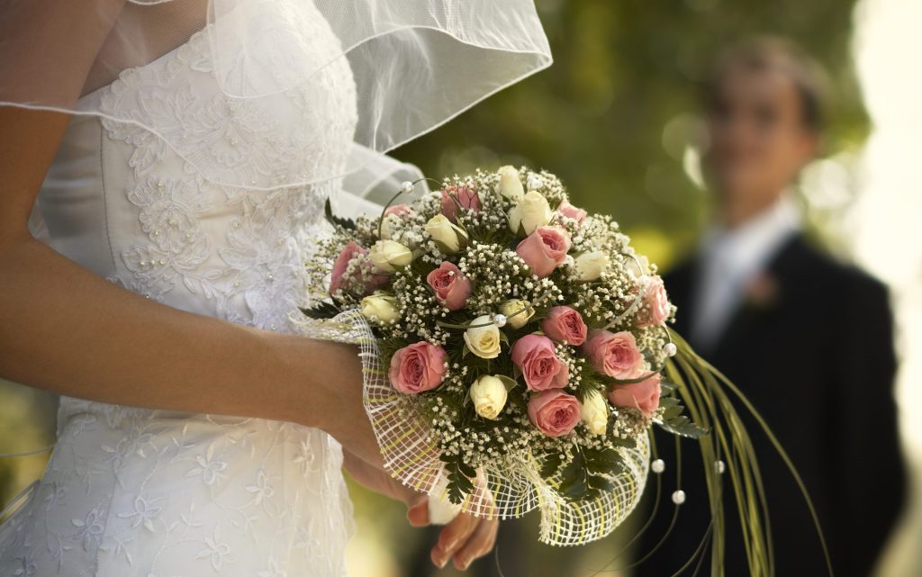bride holding a bouquet with groom looking on in the background