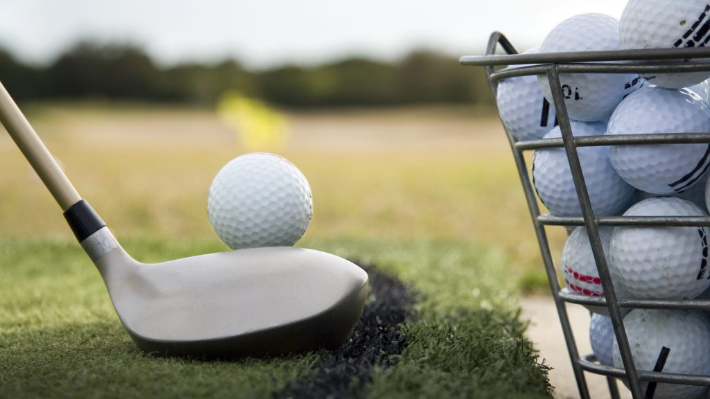 golfer lining up a practice swing next to a bucket of golf balls