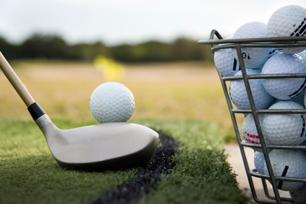 Our facilities include a driving range. A golfer lining up a practice swing next to a bucket of golf balls